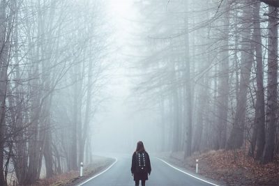Girl alone in the forest, with a road before her