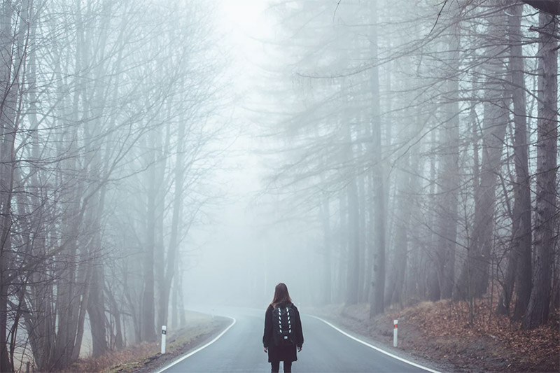 Girl alone in the forest, with a road before her